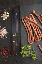 Traditional polish smoked pork sausage kabanos on a slate cutting board with salt and pepper on