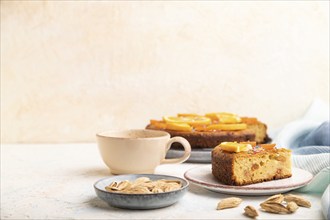 Orange cake with almonds and a cup of coffee on a white concrete background and blue linen textile.