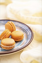 Orange macarons or macaroons cakes with cup of coffee on a white concrete background and linen