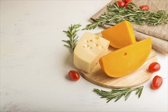 Various types of cheese with rosemary and tomatoes on wooden board on a white wooden background and