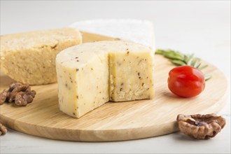 Cheddar and various types of cheese with rosemary and tomatoes on wooden board on a white wooden