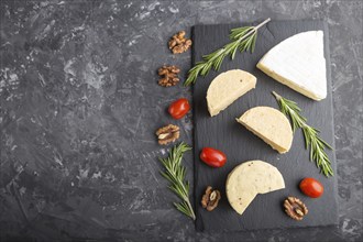 Cheddar cheese and various types of cheese with rosemary and tomatoes on black slate board on a