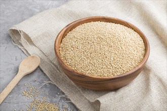 Wooden bowl with raw white quinoa seeds and wooden spoon on a gray concrete background and linen