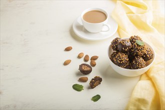 Chocolate caramel ball candies with almonds and a cup of coffee on a white wooden background and