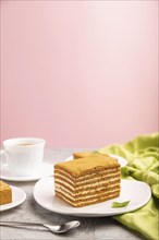 Homemade honey cake with milk cream and mint with cup of coffee on a and pink background and green