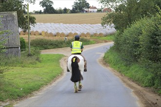 Woman riding a horse down quiet country lane, Bromeswell, Suffolk, England, UK