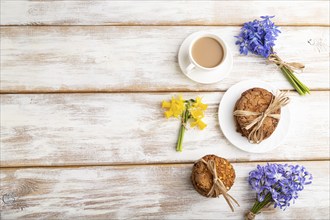 Oatmeal cookies with spring snowdrop flowers bluebells, narcissus and cup of coffee on white wooden