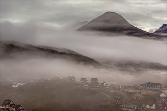 Inuit settlement, houses in the fog in front of steep mountains, Tasiilaq, East Greenland,