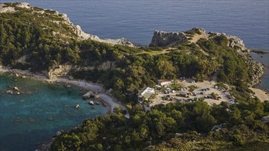 Car park and building in a rocky coastal landscape surrounded by trees and clear blue water,