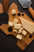 Hard cheese, parmesan, on a cutting board, cheese knife, grater, top view, no people