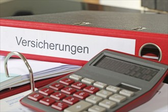 Symbolic image: Folder with insurance policies and calculator on a desk