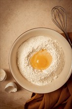 Food background, concept, plate with wheat flour, broken egg, whisk, kitchen towel, on a beige