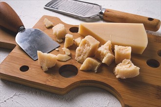 Hard cheese, parmesan, on a cutting board, cheese knife, grater, top view, no people