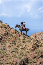 Traditional Kyrgyz eagle hunter with eagle in the mountains, hunting on horseback in front of dry