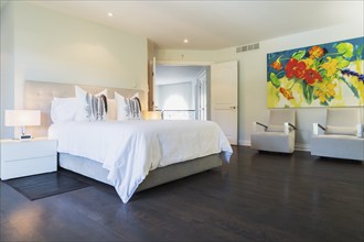 Master bedroom with queen size bed, white lacquered nightstands, upholstered armchairs and dark