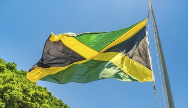 The flag of Jamaica flutters in the wind, isolated against a blue sky