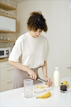 Woman cuts peeled banana on cutting board in the kitchen