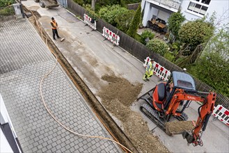 Construction workers lay fibre optic cable in trench under asphalt, cable trench, excavator,