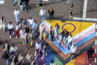 People crossing a pedestrian crossing, on a road, the road surface is colourful, in rainbow