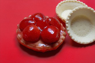 Topped strawberry tartlet and empty tartlet bases on a red background