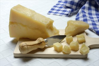 A piece of Parmesan cheese and chopped pieces of cheese on a wooden board