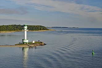 White-green lighthouse on a coast with wide water surfaces and a green buoy in the foreground,