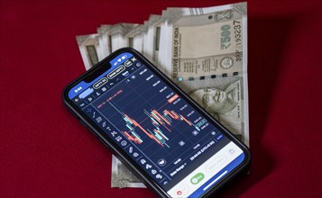 Stock market graph or chart display on a mobile phone against Indian 500 rupee paper currency note