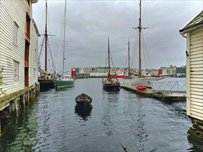 Quiet harbour scene with several boats and wooden buildings on a cloudy day, Alesund, Fylke,