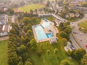 A swimming pool with outdoor area, surrounded by green spaces and trees, in an urban environment