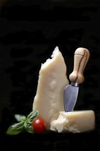 A piece of Parmesan cheese with cheese knife, basil and tomato, Italy, Europe