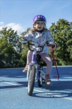 Girl with purple helmet smiling as she rides her bike on a sunny sports field