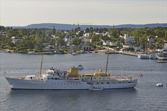 Large ship on the water in front of a coastal town with white houses and green hills, the yacht of