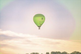 A green hot air balloon floats through the clouds high up in the sky at sunrise, Calw, Black