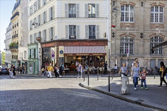 People walk past a busy corner café in an urban neighbourhood, Paris