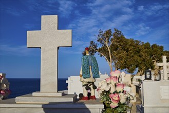 A cemetery by the sea with gravestones and crosses. In the foreground are flowers and a figure with