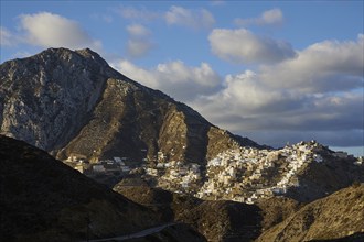 A rising village on a mountain ridge, illuminated by the sun, against a cloudy sky, Colourful