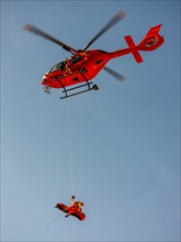 Injured person in a mountain bag with an air rescuer being winched into the rescue helicopter