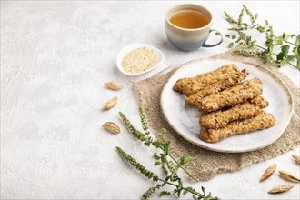 Crumble cookies with seasme and almonds on ceramic plate with cup of green tea and linen textile on