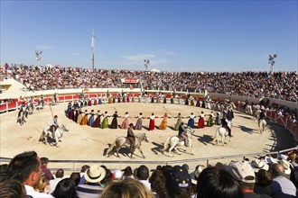 Women dance in traditional costumes and men ride horses in the arena of Les Saintes Maries de la