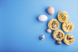 Raw uncooked tagliatelle pasta with quail eggs on a blue pastel background. top view. copy space.