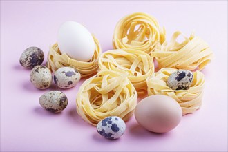 Raw uncooked tagliatelle pasta with quail eggs on a pink pastel background. side view, close up