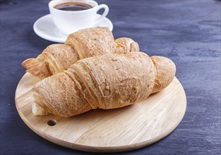 Two croissants with cup of coffee on white plate on black wooden background. closeup