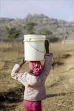 Girl carrying a heavy bucket of water on her head, Maraban Dare, 07/02/2024