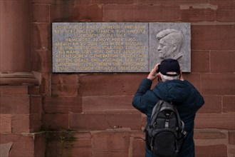 Tourist, elderly man, photographing memorial plaque and relief for John Fitzgerald Kennedy,