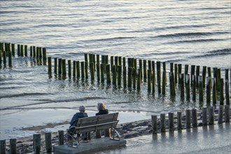 Two elderly woman on a bench on the beach, at high tide, breakwater, Netherlands