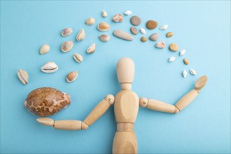 Wooden mannequin juggling sea shells on blue pastel background. close up, isolated, travel,