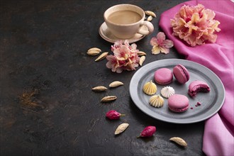 Purple macarons or macaroons cakes with cup of coffee on a black concrete background and pink