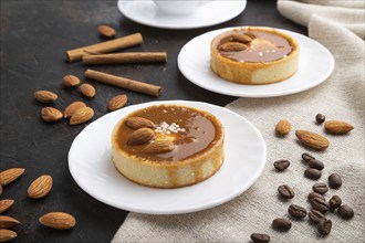 Sweet tartlets with almonds and caramel cream with cup of coffee on a black concrete background and