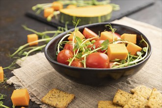 Vegetarian vegetable salad of tomatoes, pumpkin, microgreen pea sprouts on black concrete