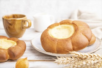 Sour cream bun with cup of coffee on a white wooden and concrete background and linen textile. Side